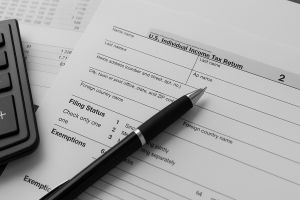 Black and white photo of calculator, pen, and spreadsheet on a desk for basic accounting services.